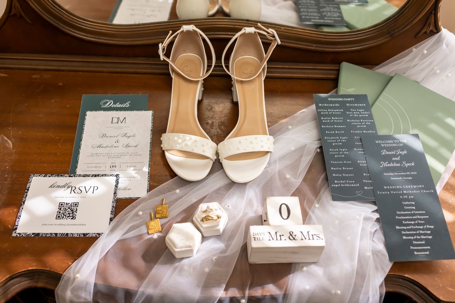 Wedding details including white heels, wedding rings, veil and program cards arranged on wooden surface.
