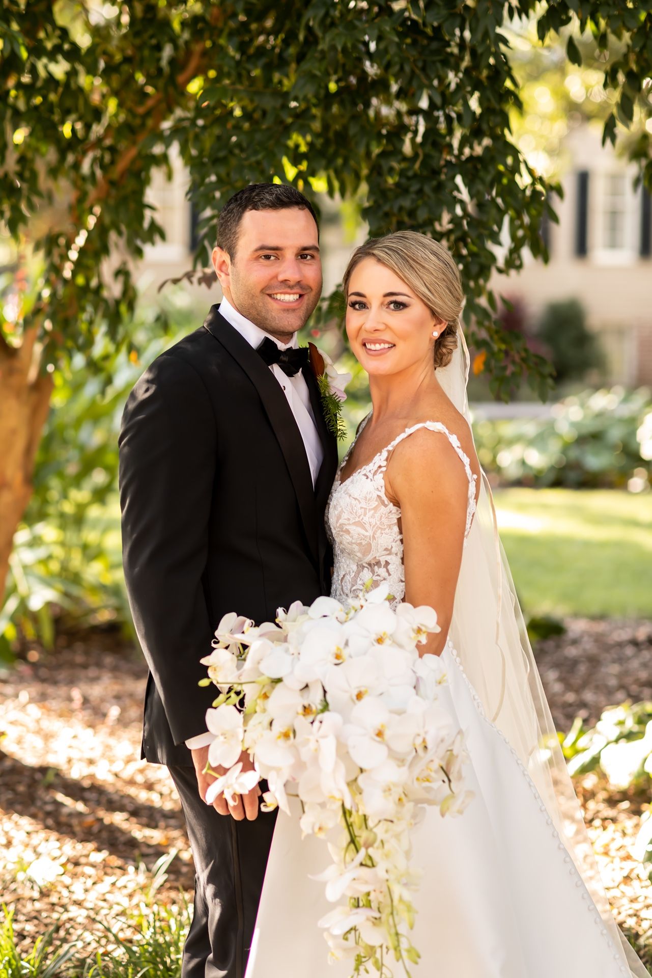 Bride and groom share romantic moments in garden setting with lush greenery and white florals.