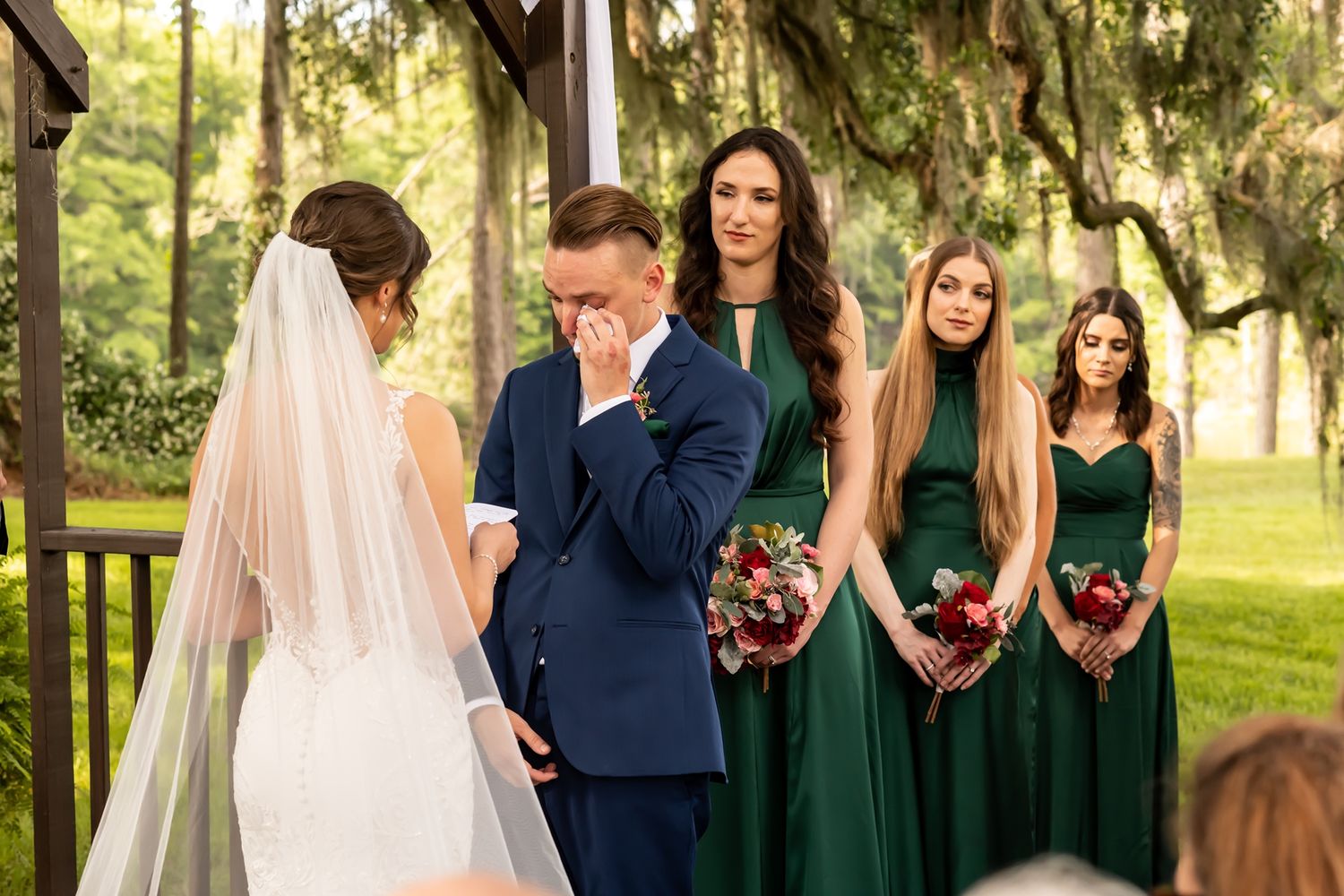 An emotional ceremony as a couple shares a touching moment while bridesmaids in emerald green dresses look on.