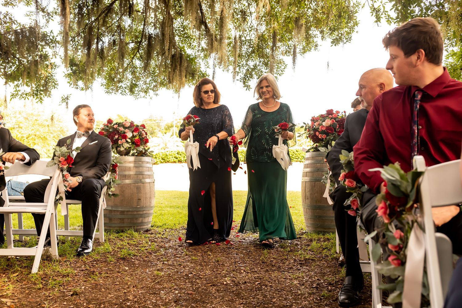 Wedding party celebrates outdoors under moss-covered oak trees at sunset.