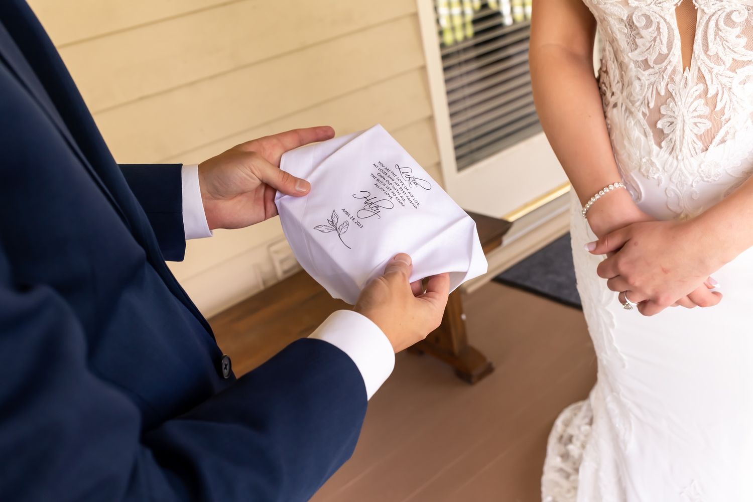 A person in a navy suit holds written vows while standing next to someone wearing a white lace wedding dress.