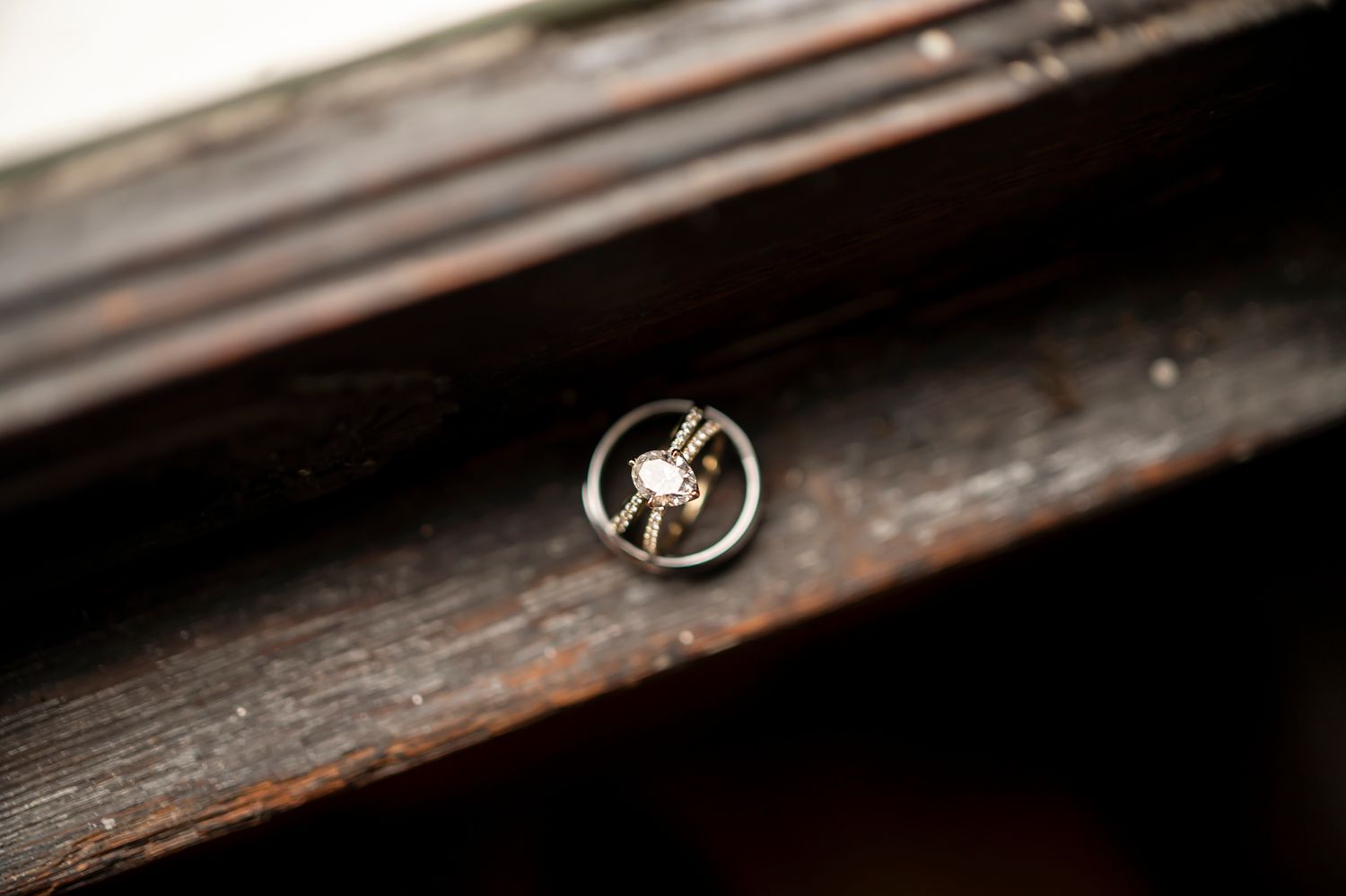 A closeup macro shot of a small silver spider-shaped insect pin against a dark wooden surface in soft focus.