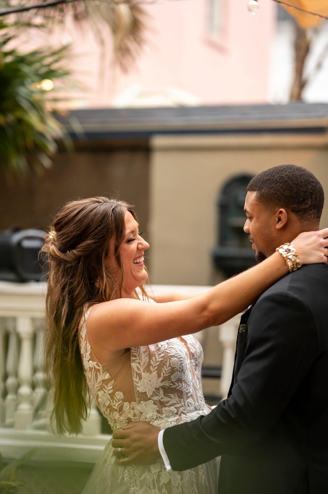 A bride in a lace wedding dress and groom in a black suit embrace while dancing during an outdoor celebration.