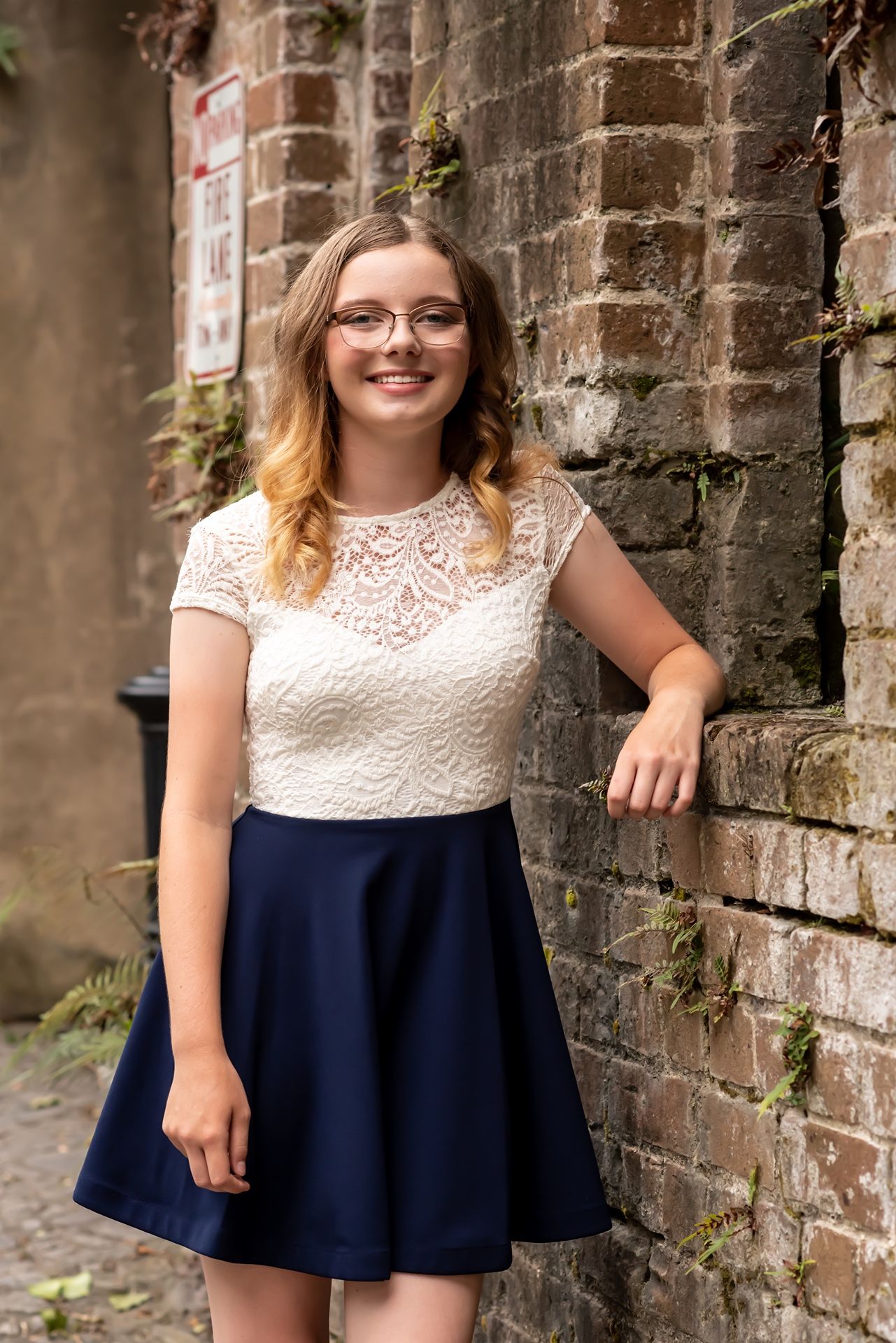 A dress outfit featuring a white lace bodice and navy blue skirt photographed against a rustic brick wall background.