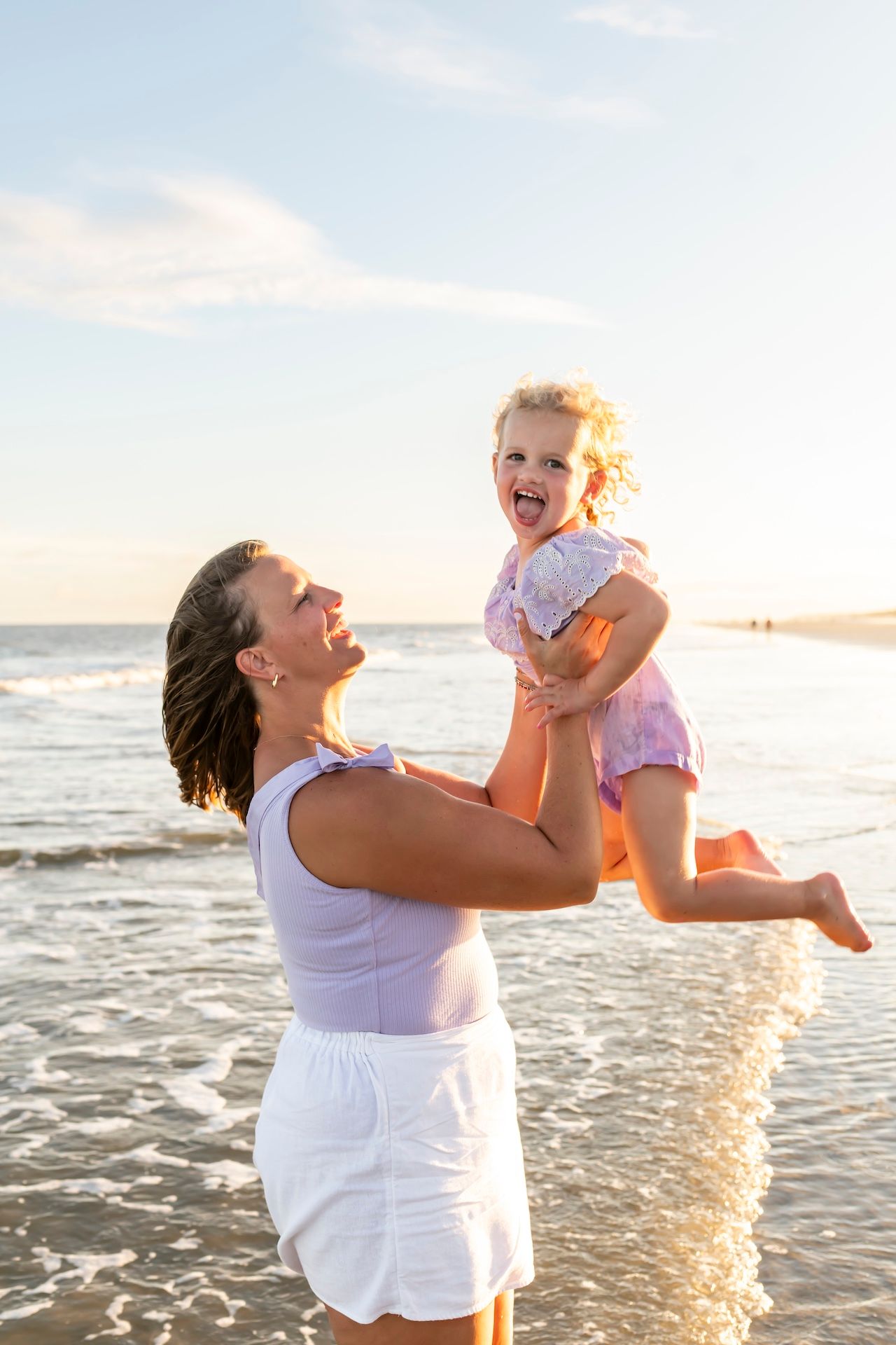 A joyful moment shared between a caregiver and child playing in the ocean at sunset.