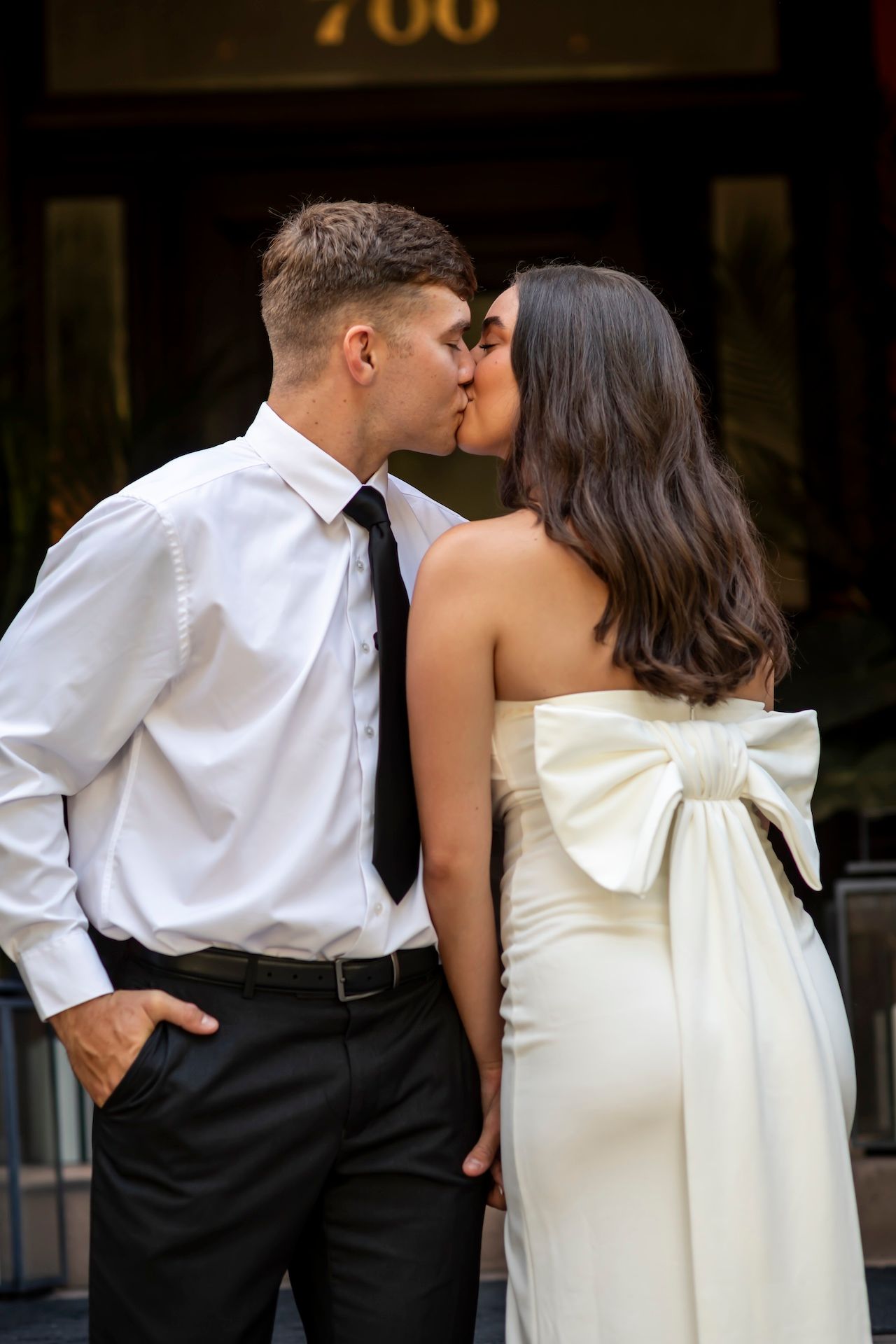 A couple sharing a romantic kiss, with the bride in an elegant white dress with a large bow detail and groom in formal attire.