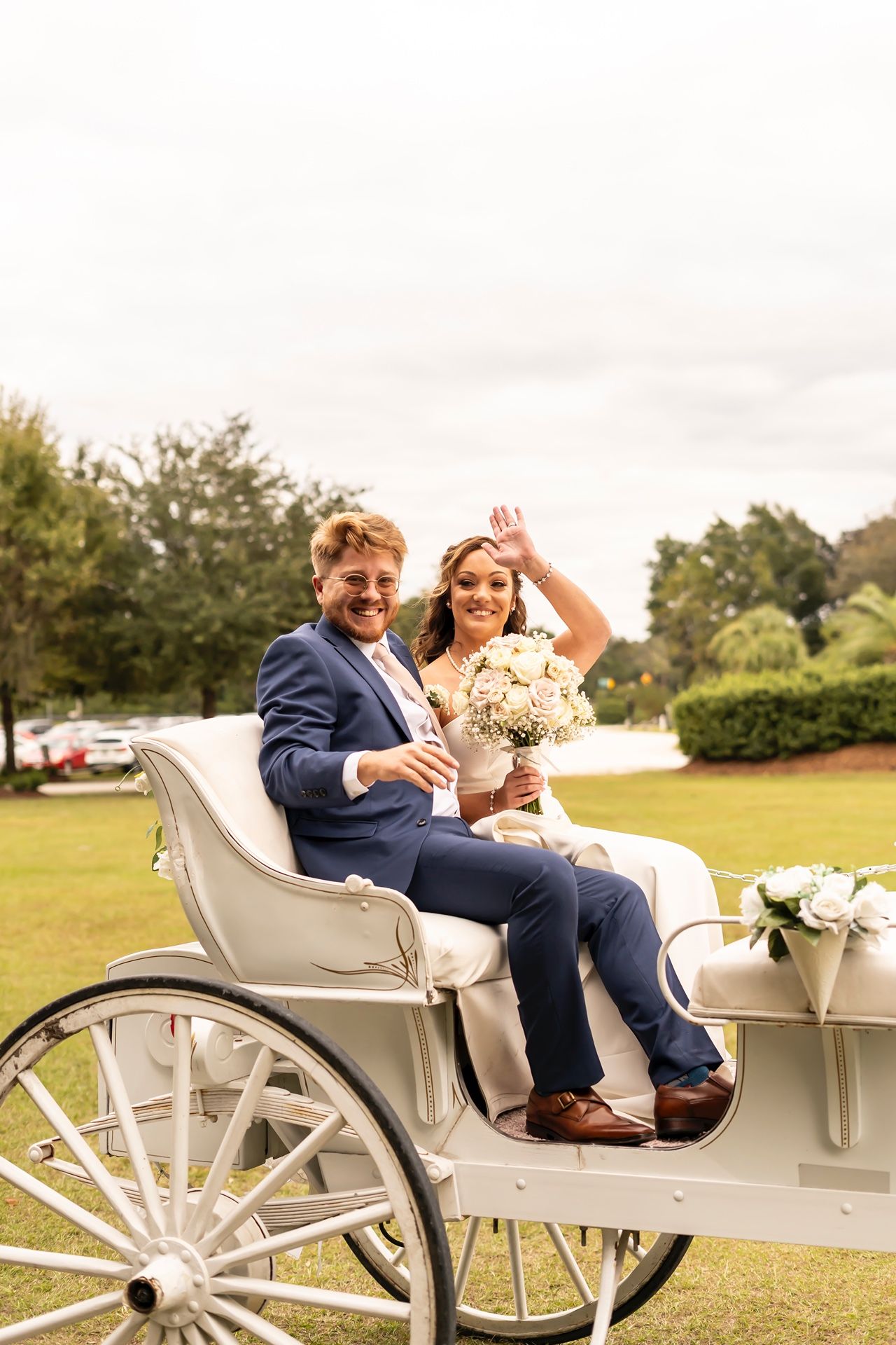Newlywed couple celebrates in a romantic white horse-drawn carriage on a lush green lawn during their wedding day.