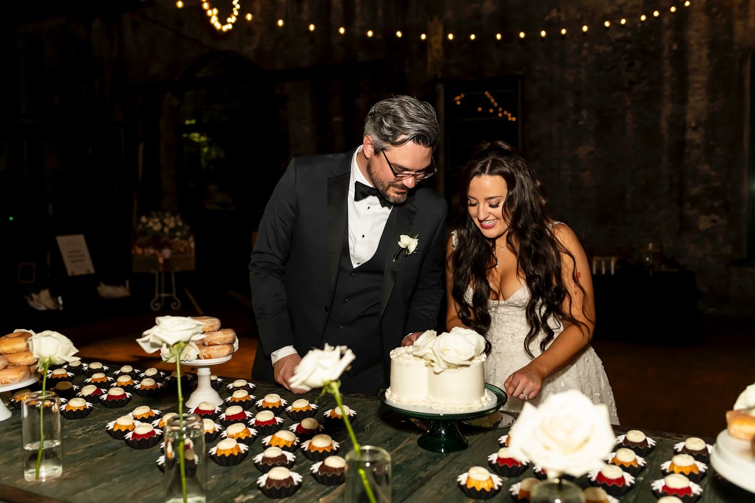 Happy newlyweds cut their elegant three-tier wedding cake adorned with flowers at their romantic reception.