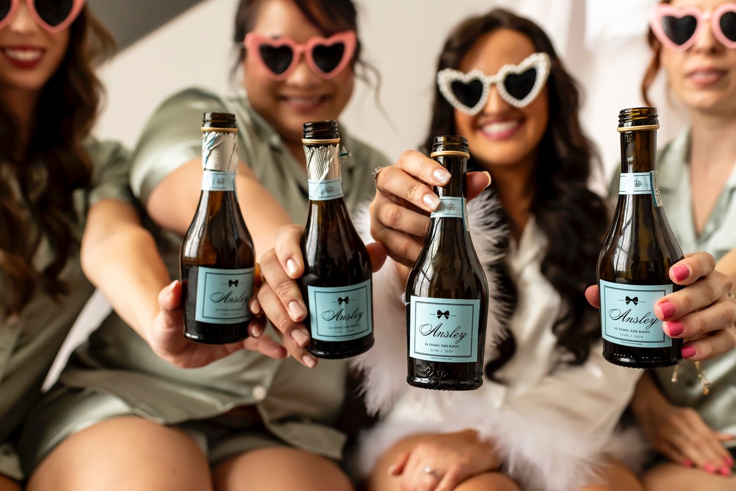 Friends toasting and clinking wine bottles together in a celebratory gathering outdoors.