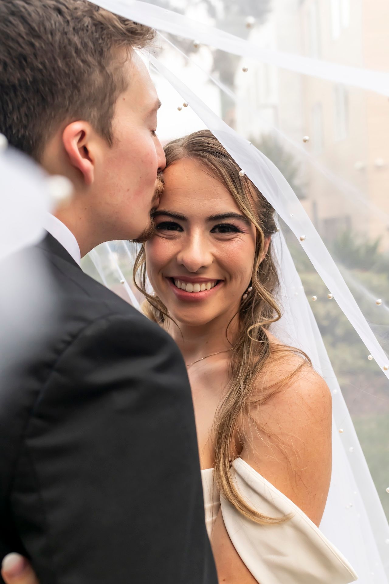Beautiful bride in a white dress smiles radiantly while sharing an intimate moment with her groom on their wedding day.