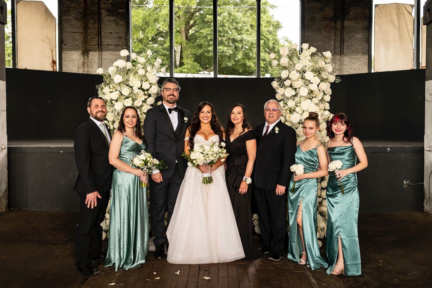 Formal wedding party poses together in front of white floral arrangements in an elegant venue setting.