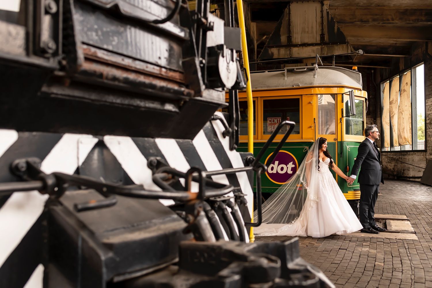 A couple poses at a vintage train station platform with an orange railcar in the background.