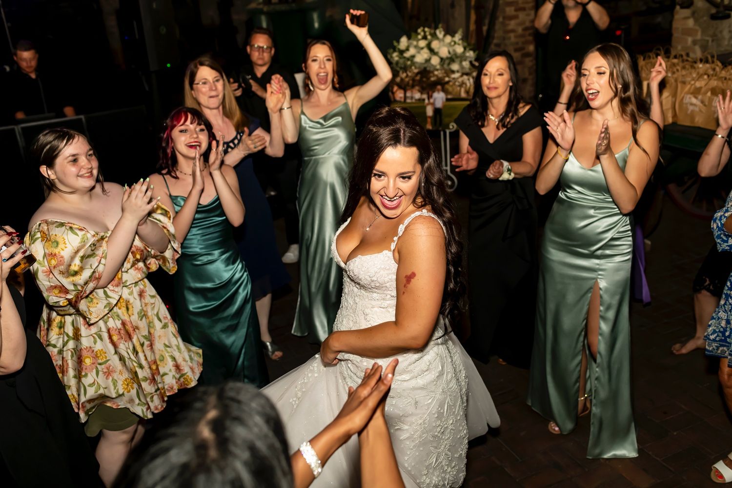 Energetic group of wedding guests and bridesmaids in green dresses dance together on the dance floor at an evening reception.