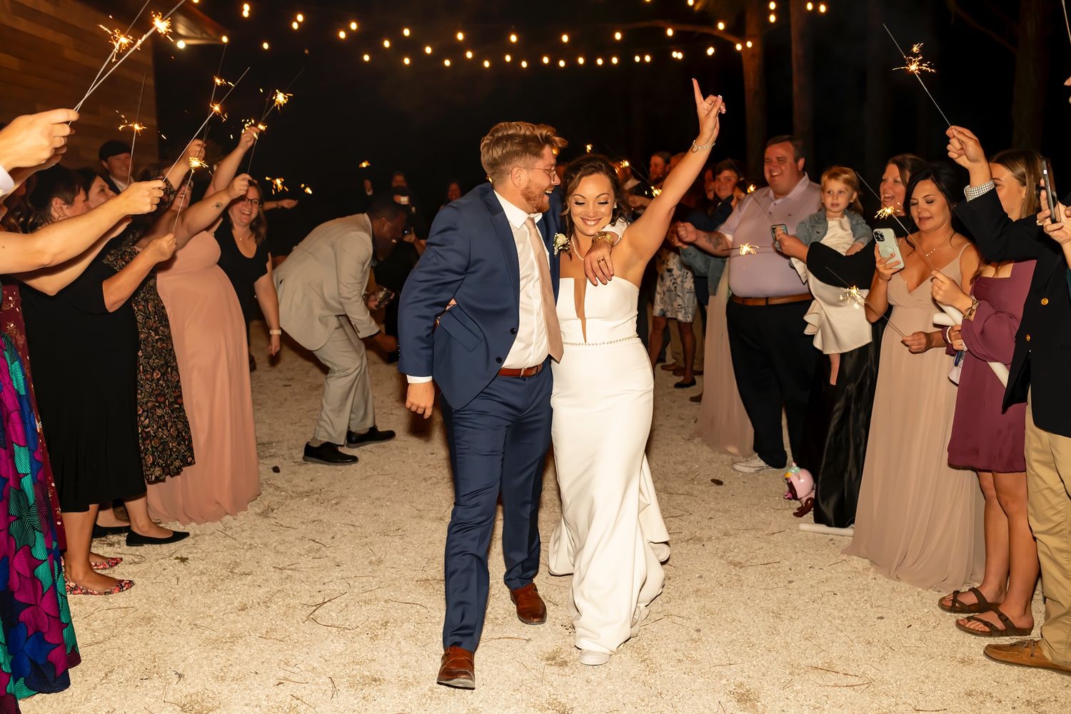 Wedding reception guests dancing on dance floor under string lights at outdoor evening celebration.