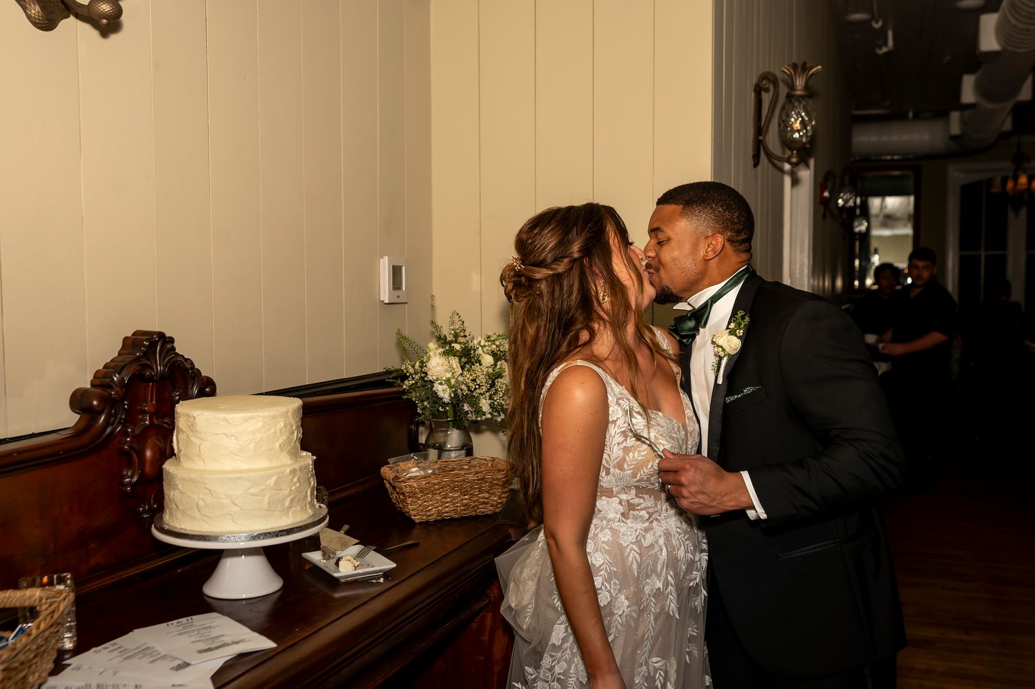 A couple shares an intimate moment next to their wedding cake at their reception celebration.