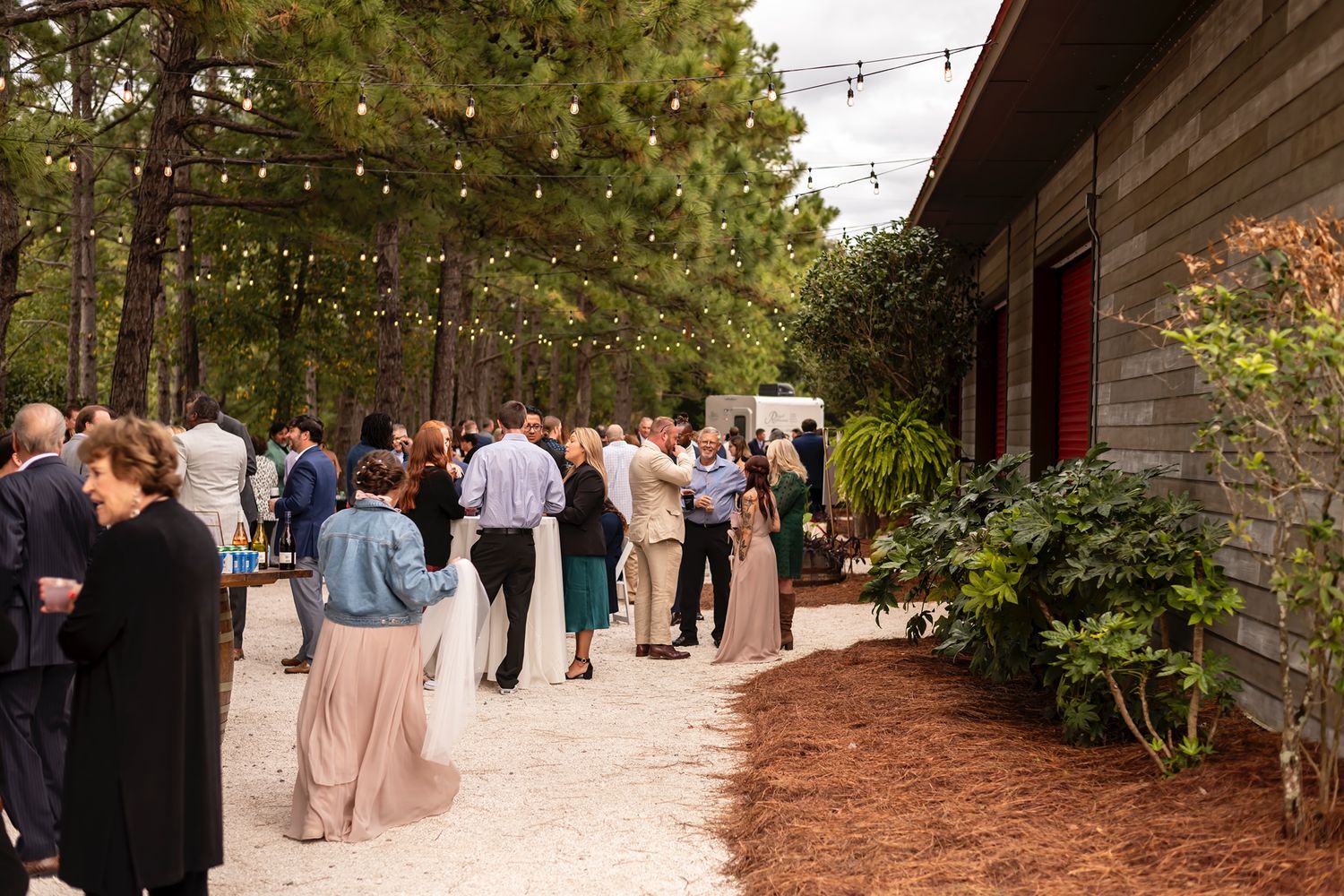 Outdoor string lights illuminate a rustic covered walkway decorated for a wedding reception gathering.