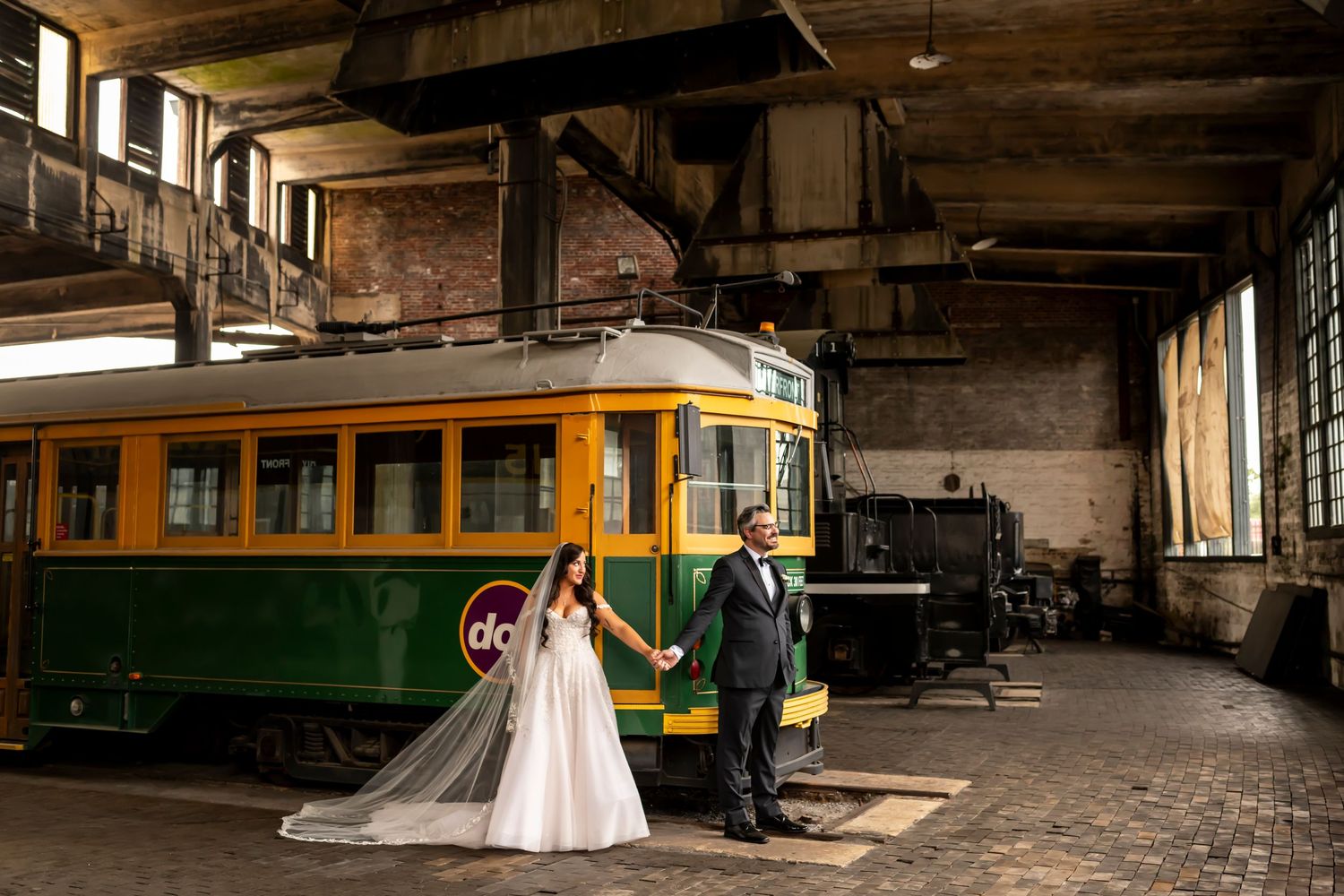 Wedding couple posing inside vintage streetcar depot with antique trolley at Georgia State Railroad Museum.