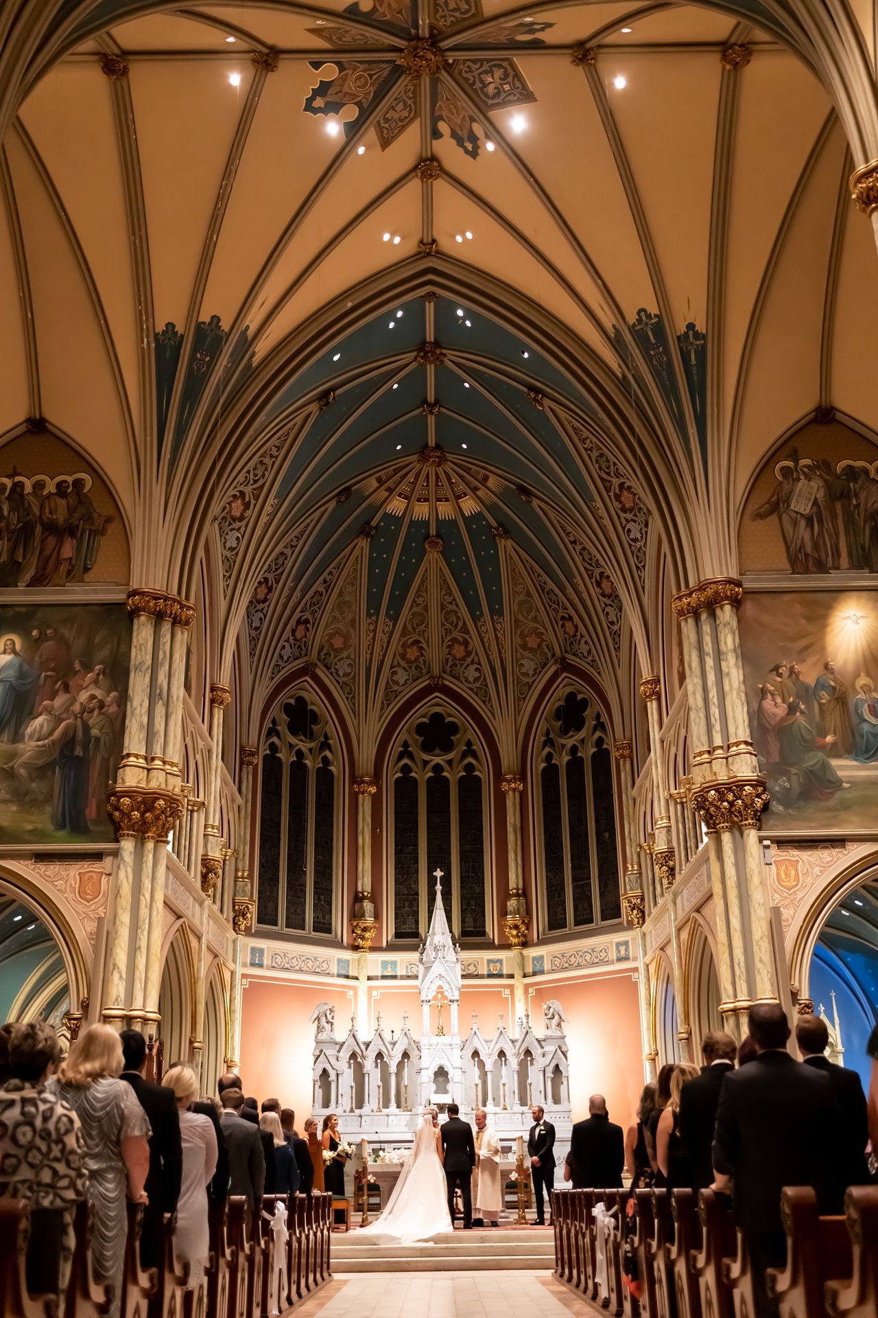 A cathedral wedding ceremony under soaring Gothic arches with vaulted ceilings and ornate architectural details.