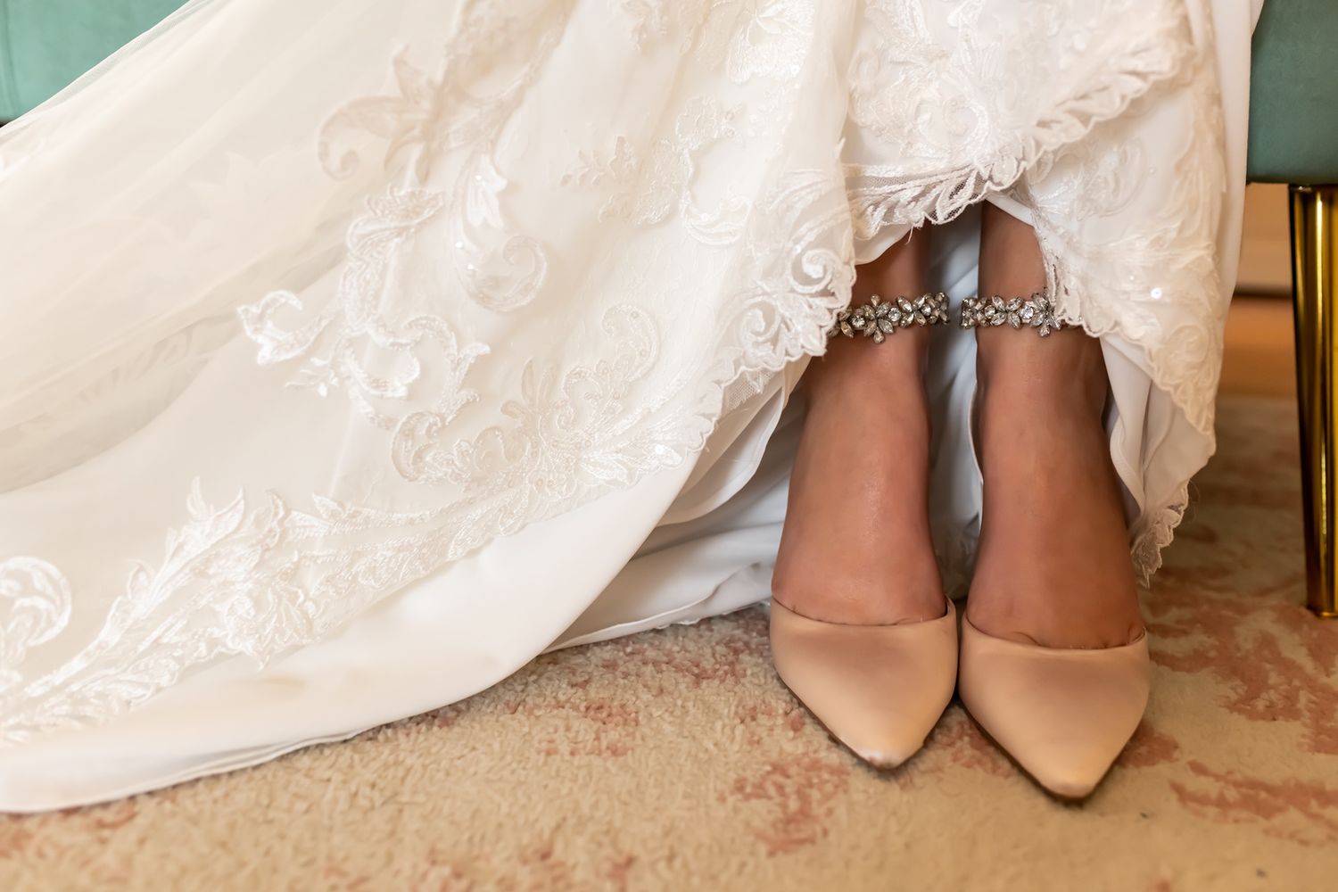 Closeup of a bride's feet wearing elegant nude heels with her white wedding dress cascading around them.