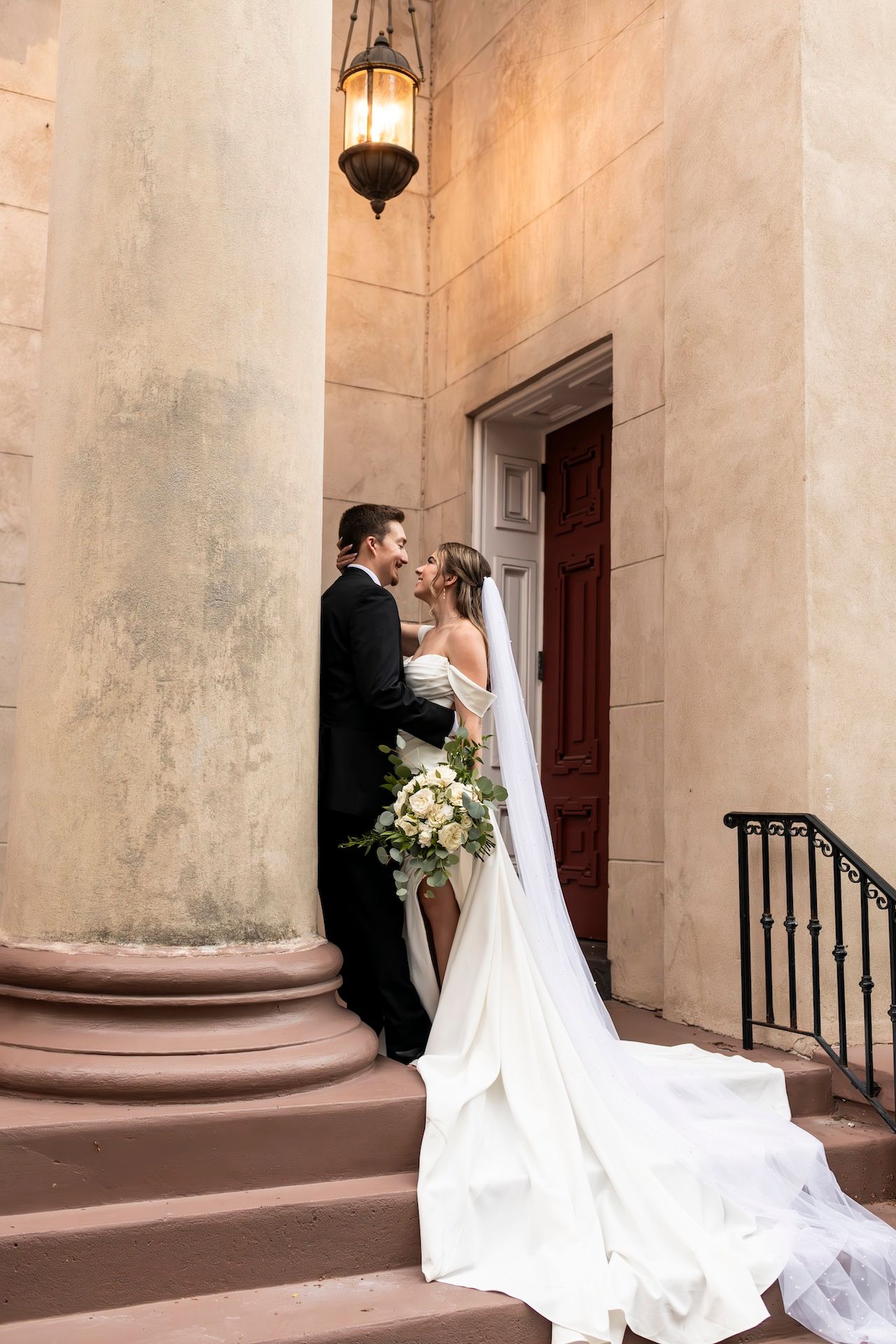 Elegant couple sharing a romantic moment on stone steps at their wedding with a vintage lantern overhead.