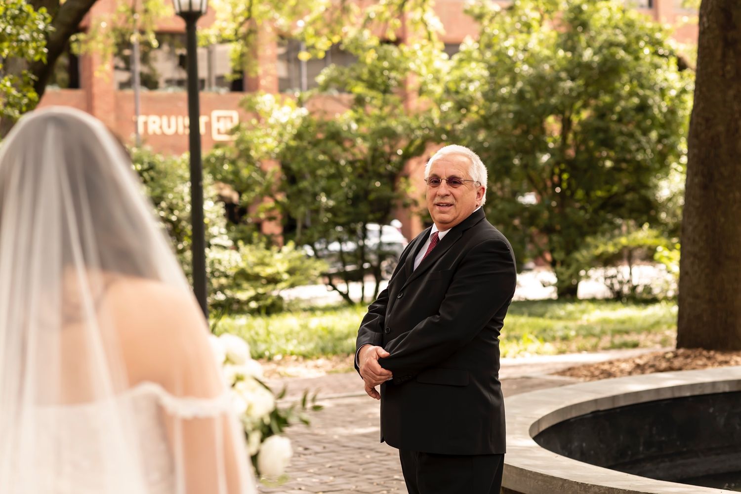 First look wedding moment between a bride in a veil and someone in formal black attire in a garden courtyard setting.