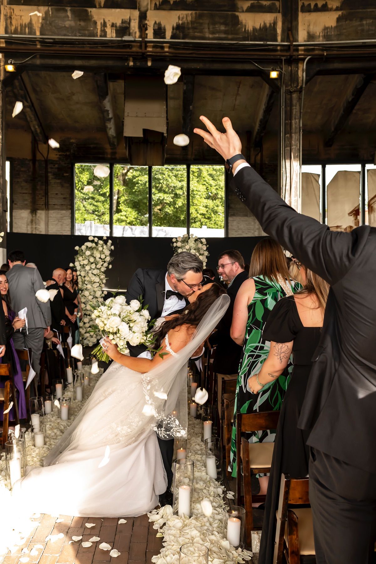 Couple shares a romantic dip and kiss during their wedding ceremony in an indoor venue decorated with white flowers and candles.
