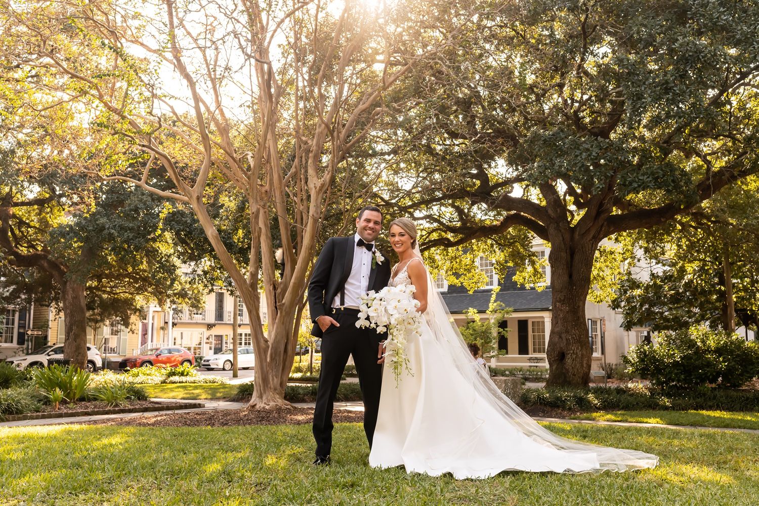 A romantic couple poses under sunlit oak trees in a scenic park setting at golden hour.