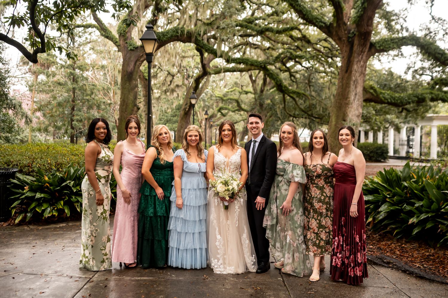 Wedding party poses together under moss-draped oak trees in a southern garden setting with beautiful formal dresses.