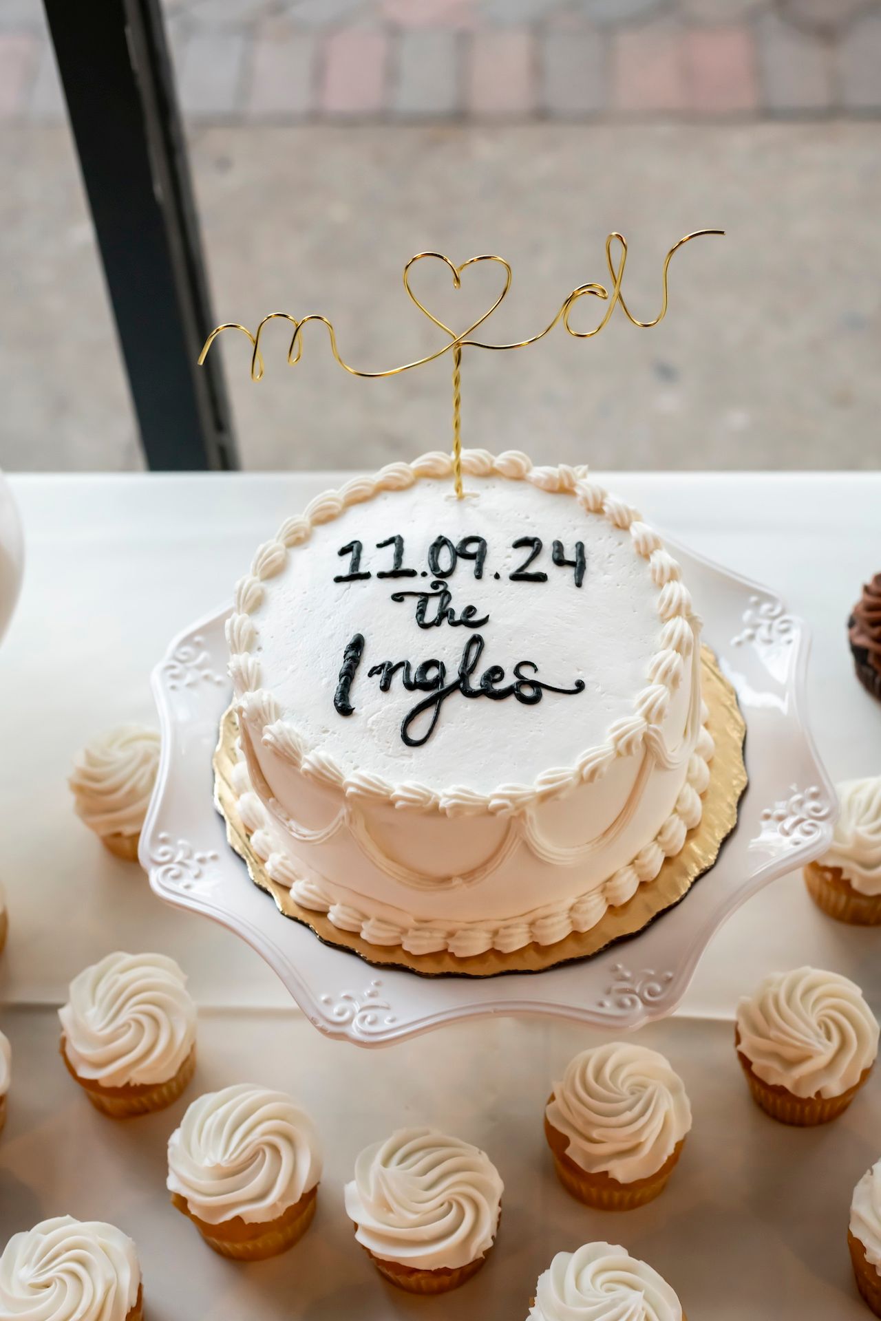 A white wedding cake with gold wire topper and the date