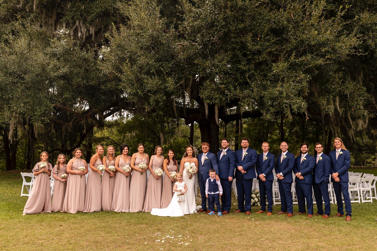 Wedding party stands in line wearing coordinated pink and navy outfits at outdoor garden venue.