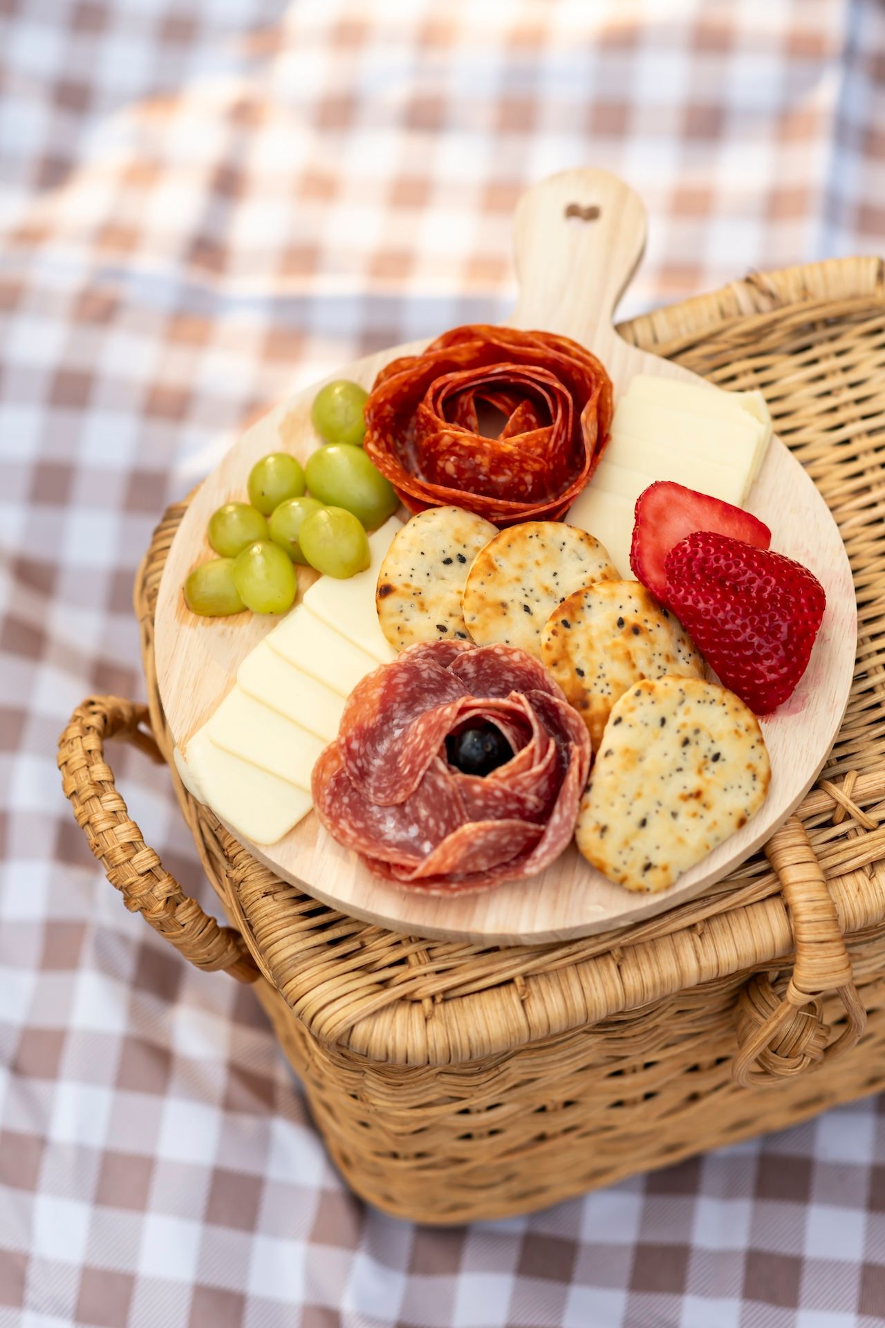 Charcuterie board with meats, cheese, grapes and crackers served on a wooden plate over checkered tablecloth.