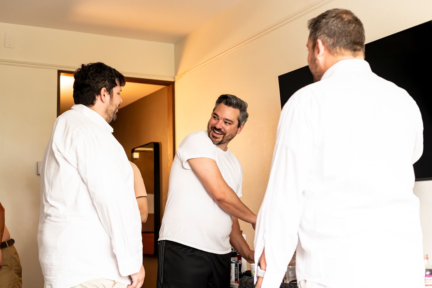 Three people wearing white clothing stand in conversation in what appears to be a bright interior room setting.