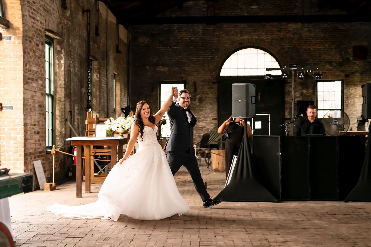 A couple dances in an elegant industrial venue with exposed brick walls and high ceilings during their wedding celebration.