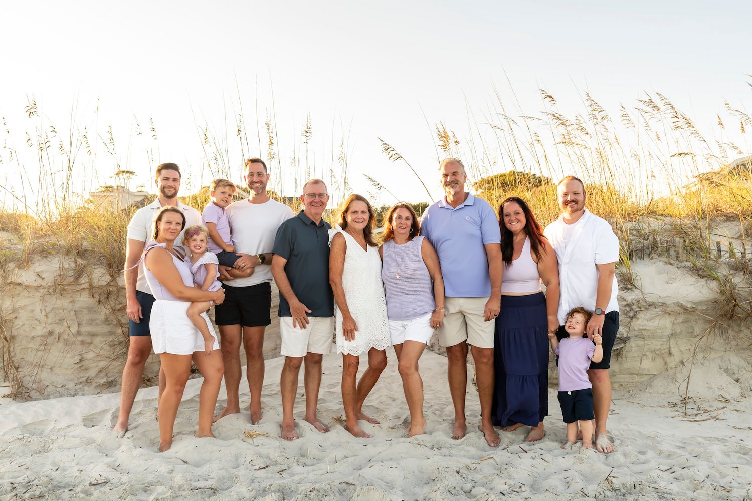 A group of people dressed in white and blue stand together on a sandy beach dune at golden hour.