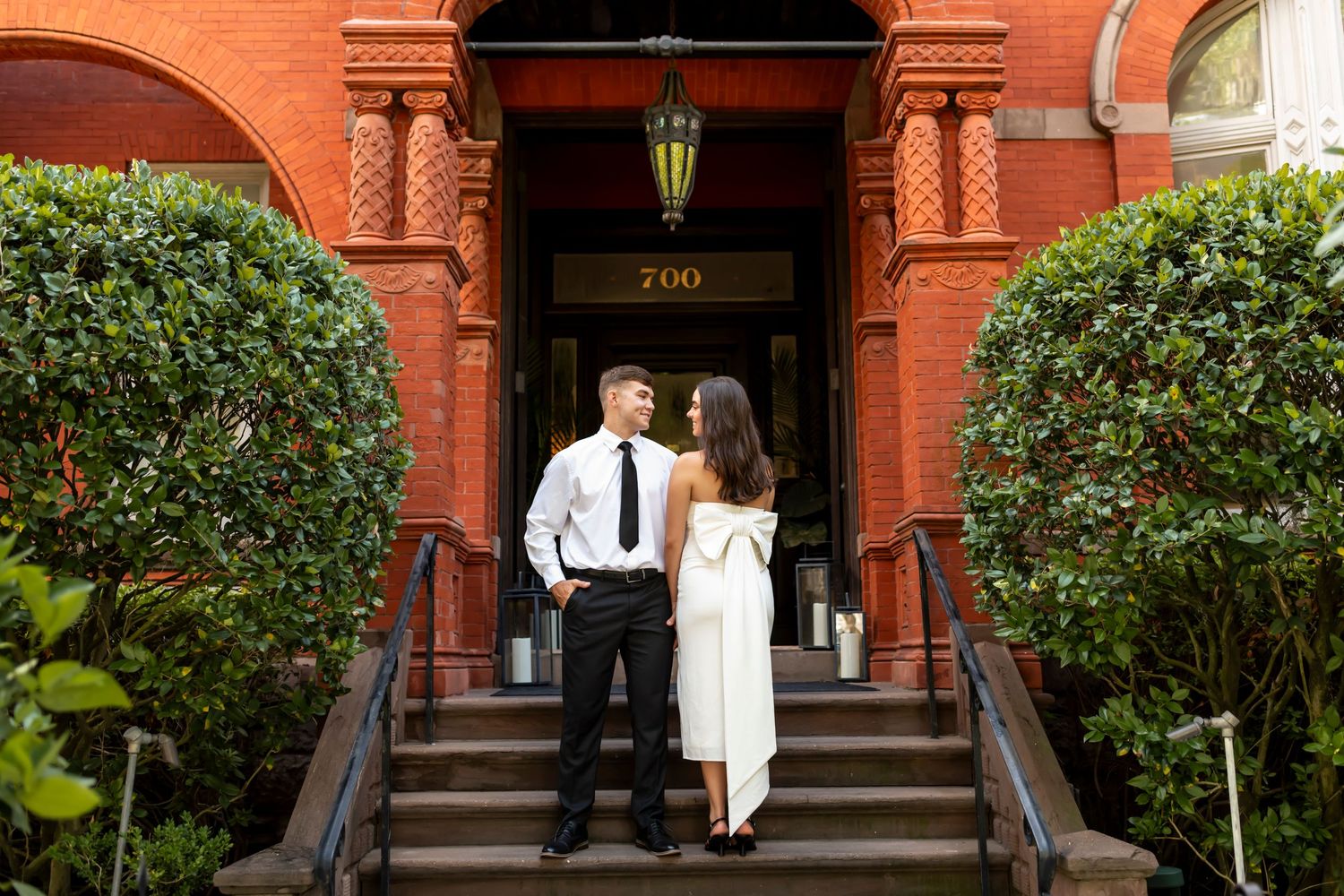 A couple stands in front of brick mansion for their engagement photos.