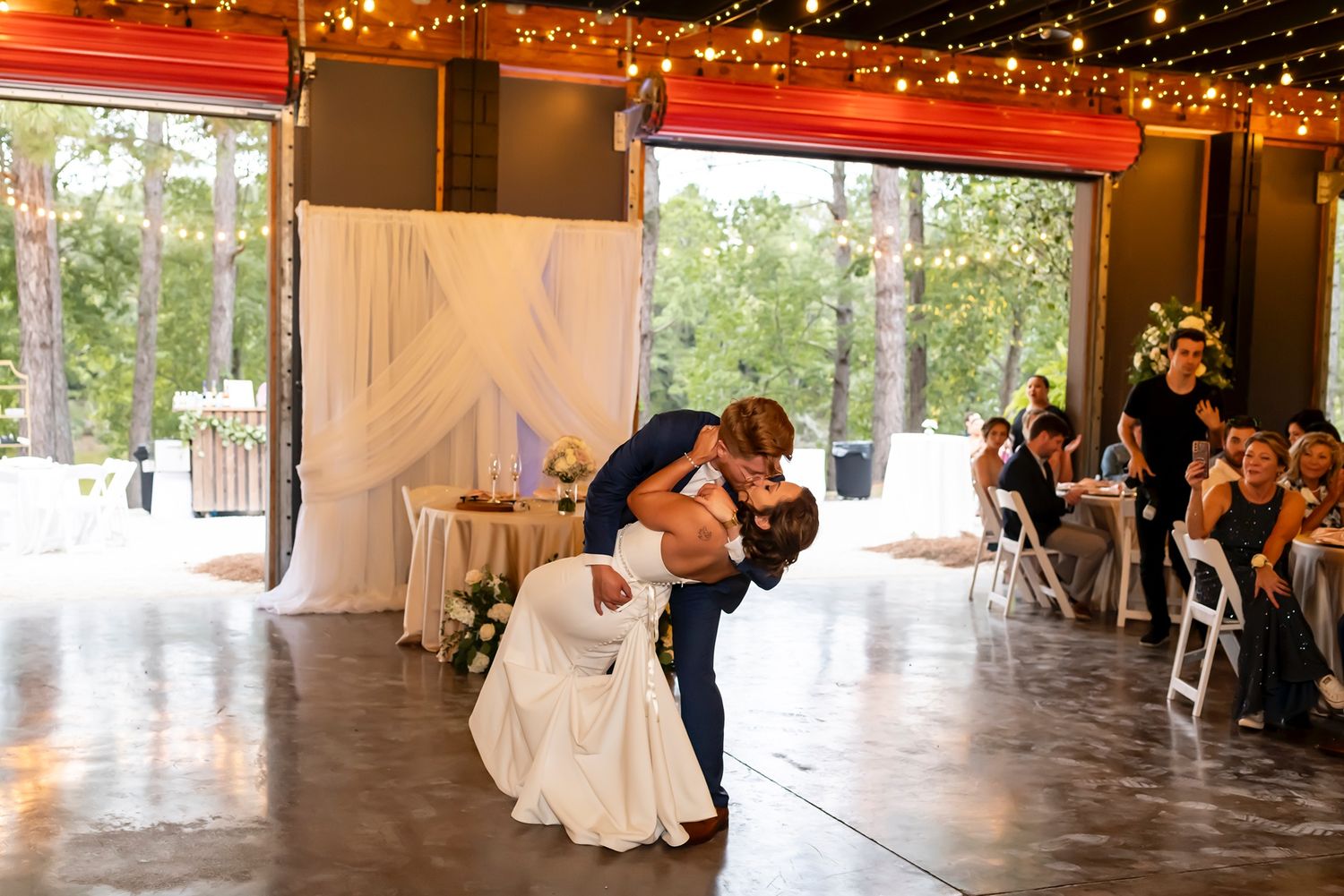 A rustic barn reception venue decorated with twinkle lights and white draping for an elegant wedding celebration.