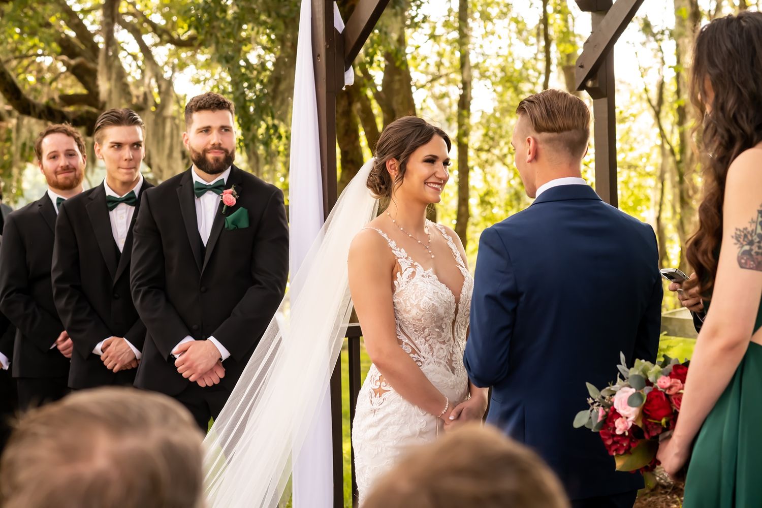 Wedding party gathers for outdoor photos under tree canopy at sunset during an elegant fall ceremony.