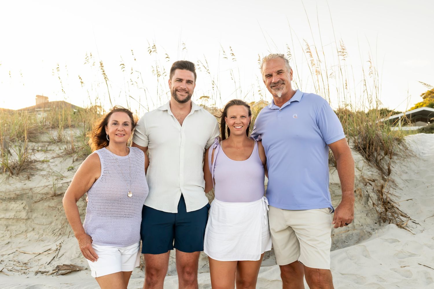 Group of people standing together and smiling in front of coastal sand dunes at sunset.