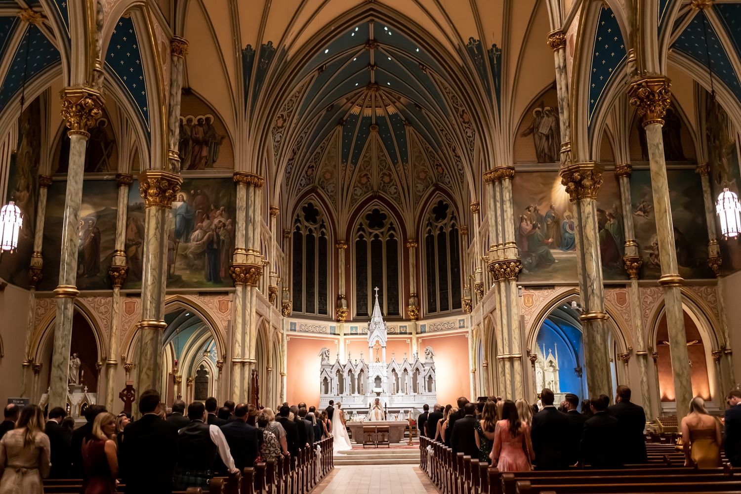 Beautiful Gothic cathedral interior with vaulted ceilings and arches illuminated during a crowded evening ceremony.
