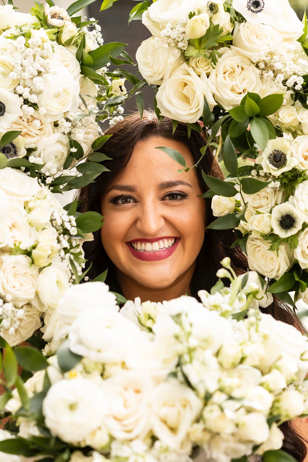 A joyful smile peeks through a lush arrangement of white roses, anemones and delicate floral blooms.