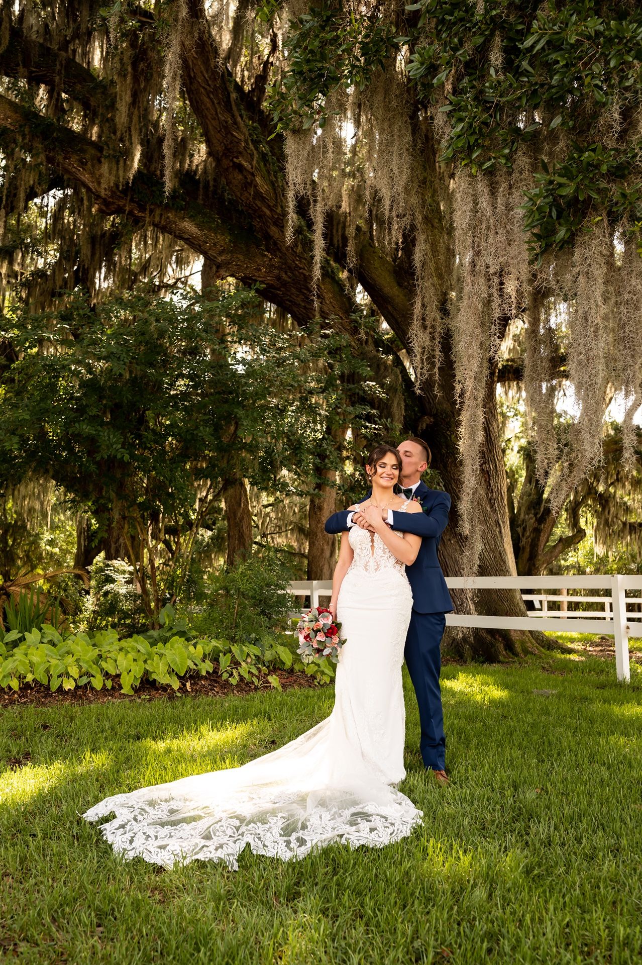 A romantic wedding photo capturing a couple embracing under majestic Spanish moss draped oak trees in a Southern garden.