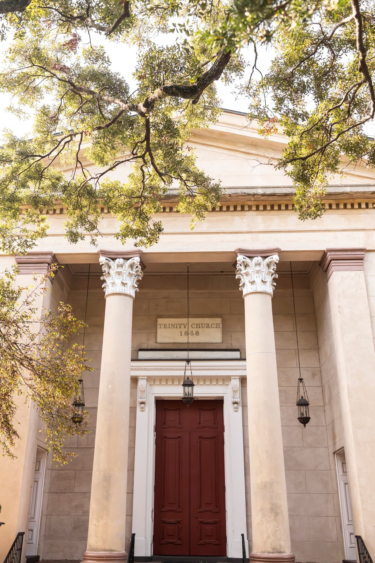 Classic colonial architecture featuring white columns and a dark red door under an ornate cornice with hanging lanterns.
