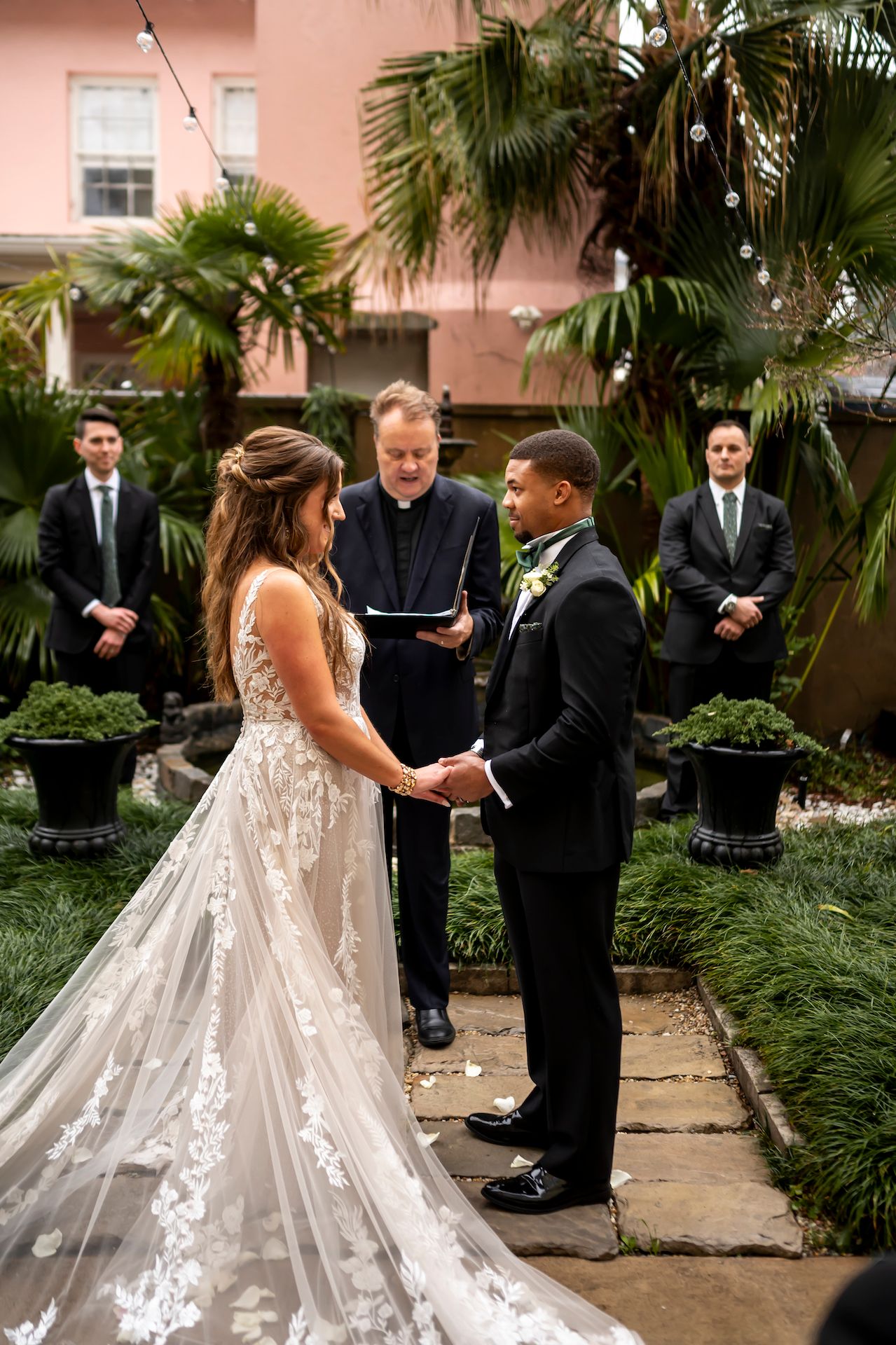 Couple gets married during outdoor ceremony in lush garden courtyard with palm trees and tropical plants.