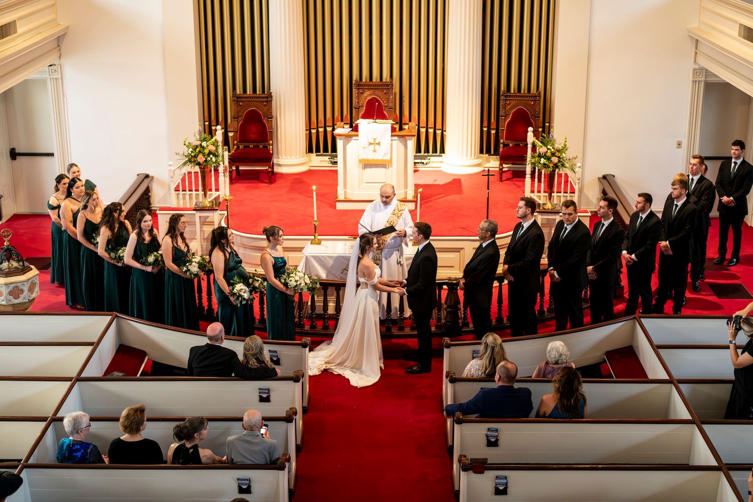 Overhead view of a wedding ceremony in a traditional church with red carpet and white pews and elegant decor.