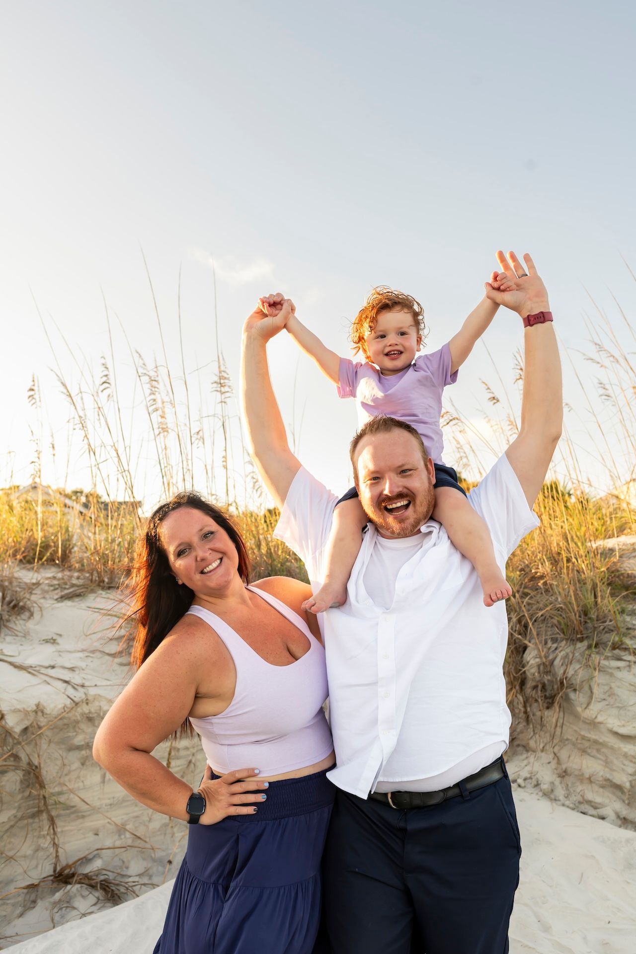 A joyful family poses together on sandy dunes at sunset with tall grass in the background.