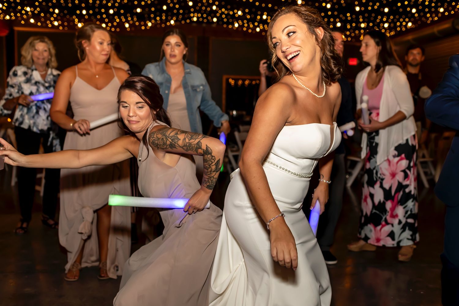 Wedding guests dance and celebrate on the dance floor under twinkling lights during an evening reception.