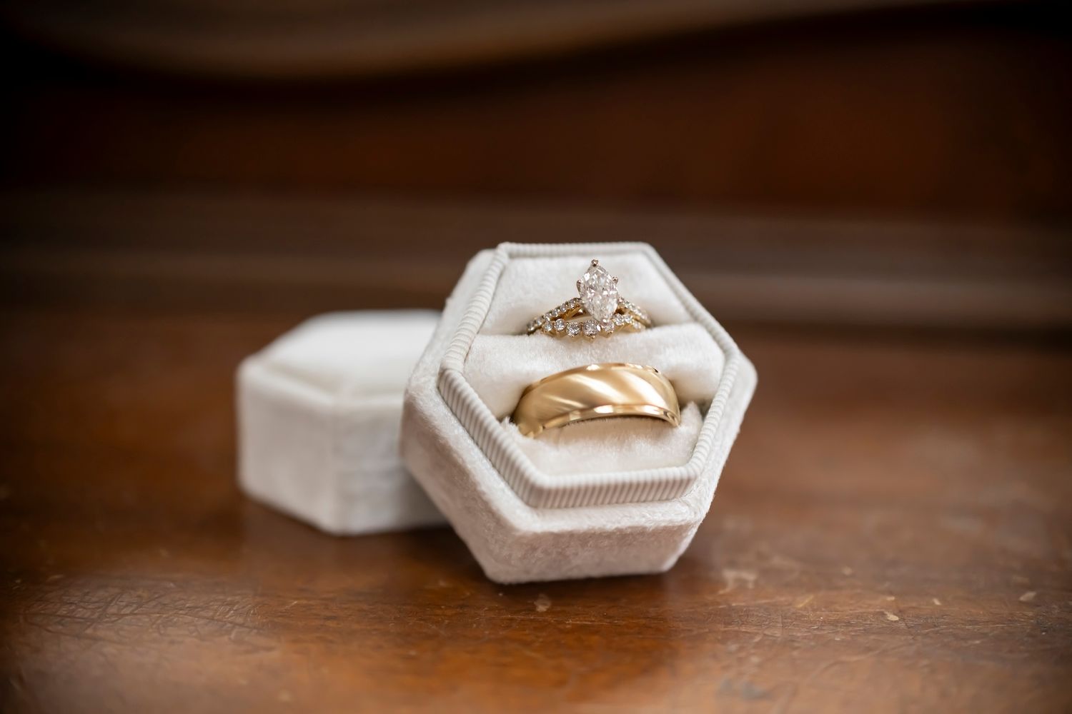 Two gold wedding rings nestled in a white hexagonal ring box with velvet lining on a wooden surface.