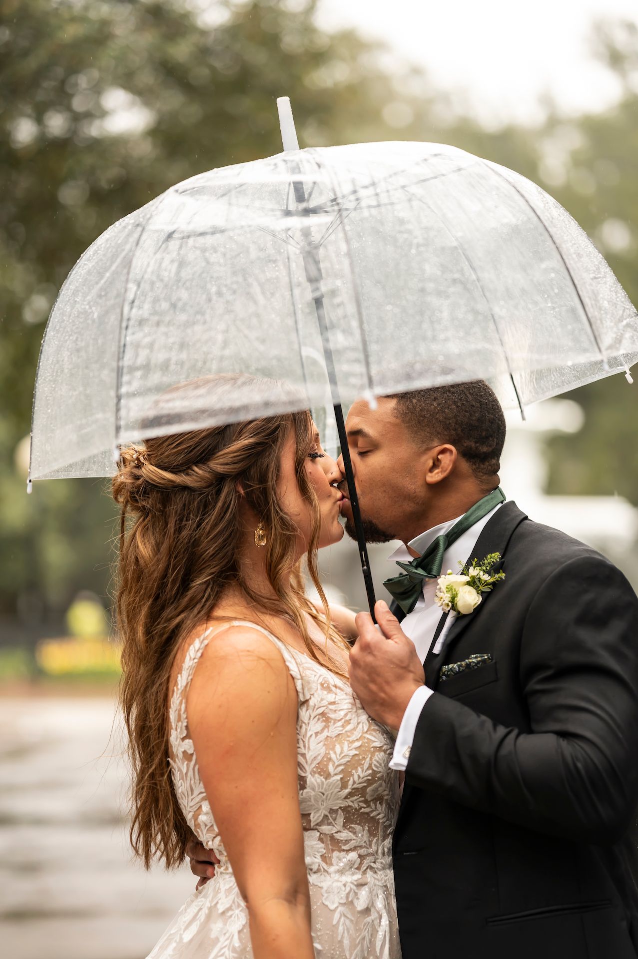 Romantic couple sharing intimate moments under white umbrella in the rain during wedding photoshoot.