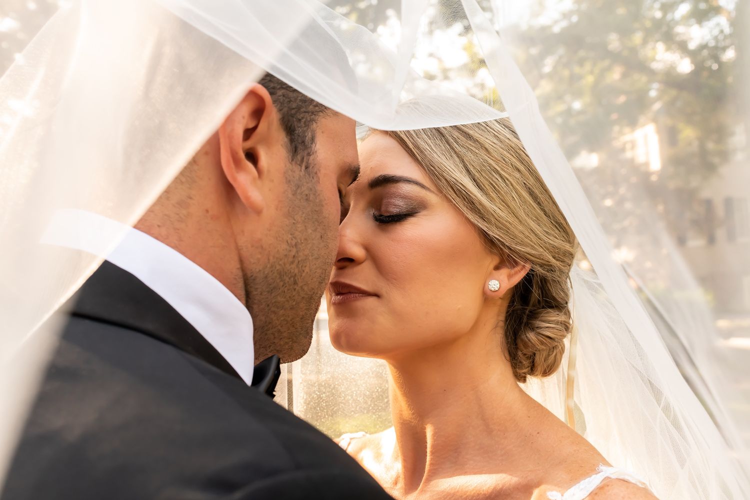 Romantic couple shares intimate moments under a veil in soft golden light during their outdoor wedding photoshoot.