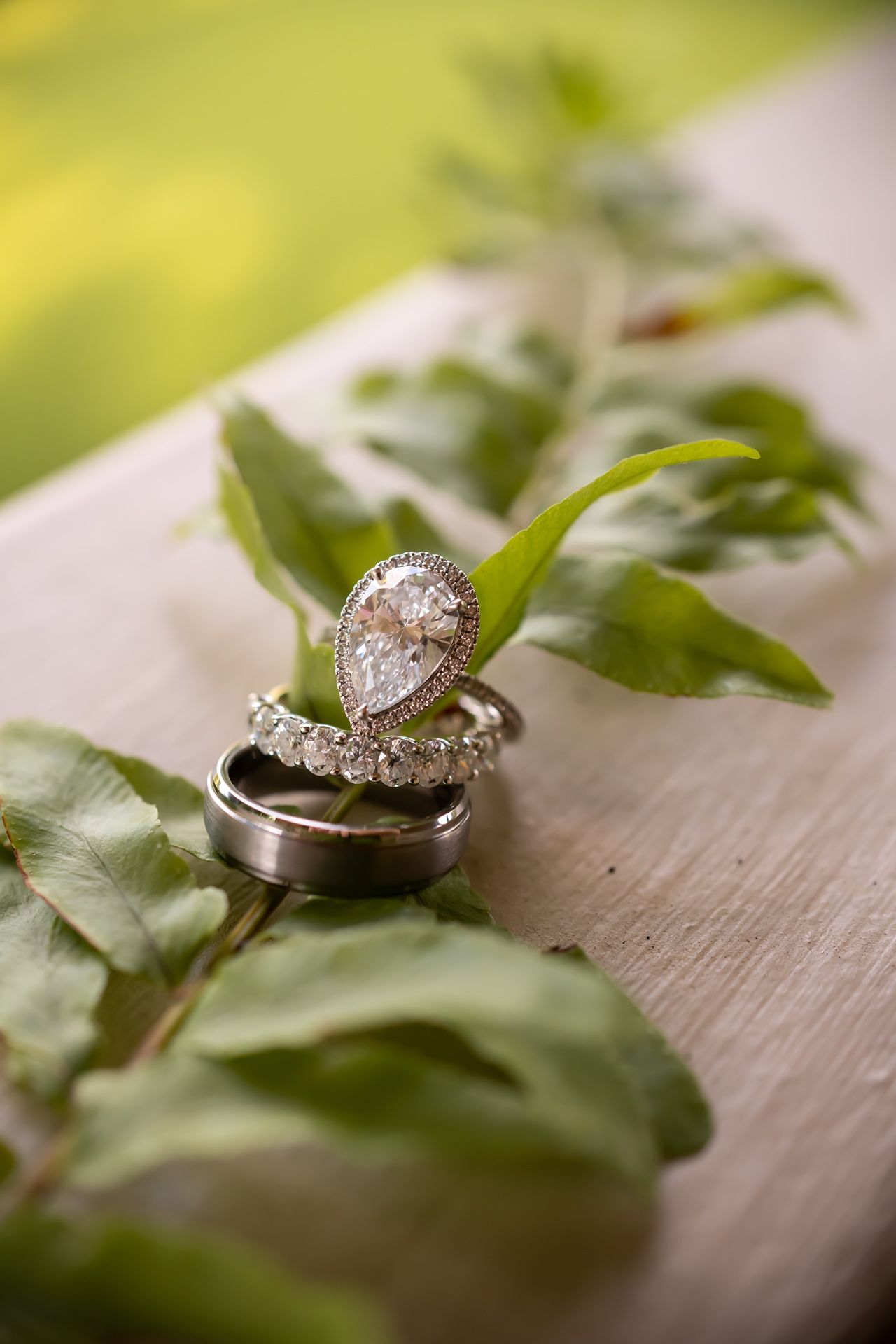 Elegant diamond engagement ring and wedding band displayed on wooden surface with green leaves for wedding detail photography.